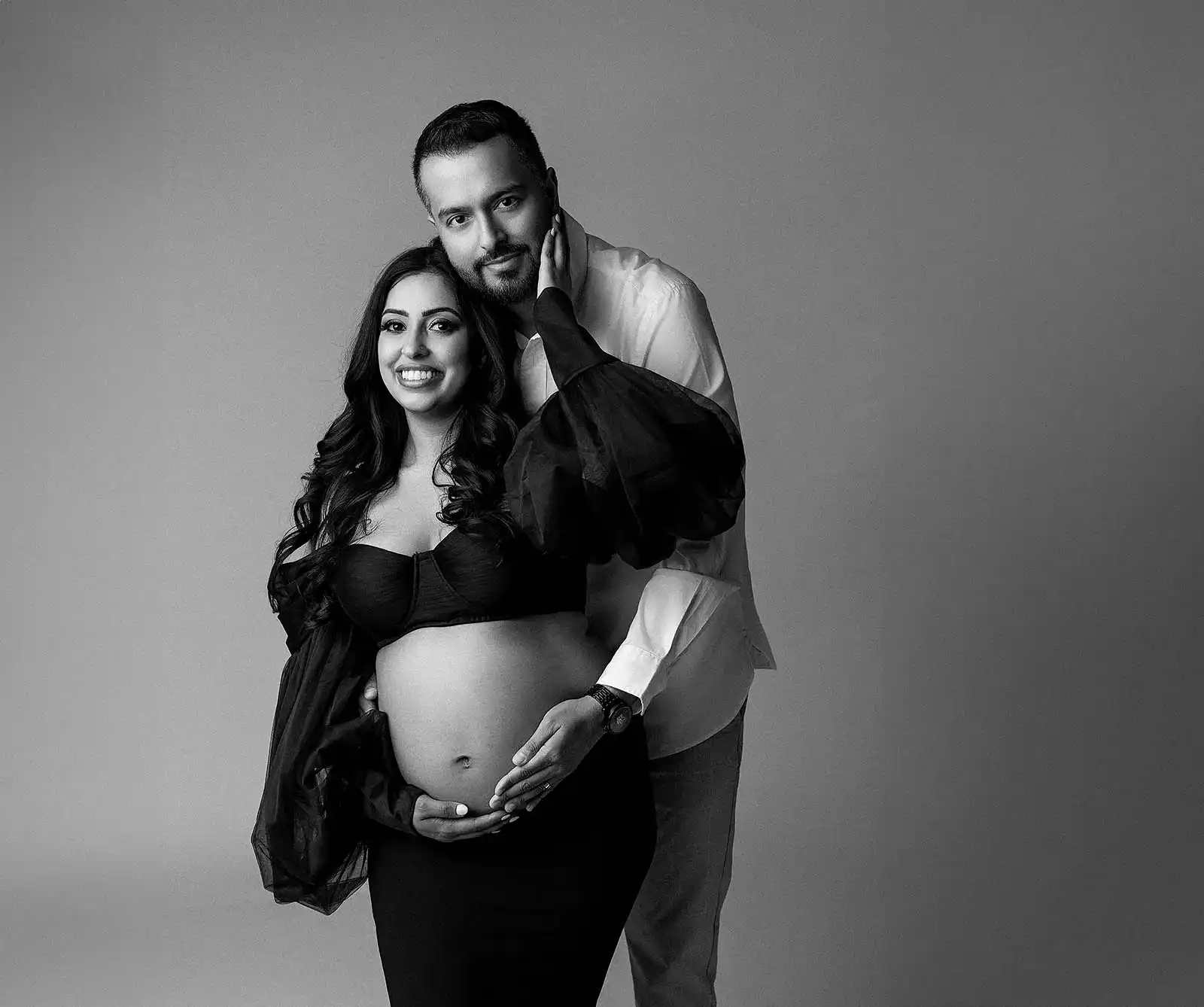a couple pose against a grey backdrop during a Surrey Maternity photoshoot